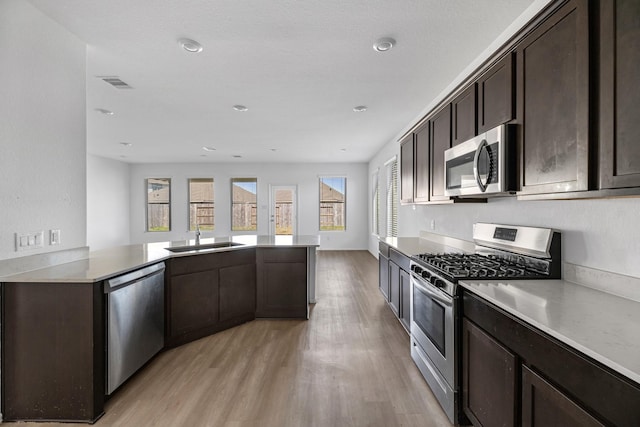 kitchen featuring light wood finished floors, appliances with stainless steel finishes, a sink, dark brown cabinetry, and a peninsula