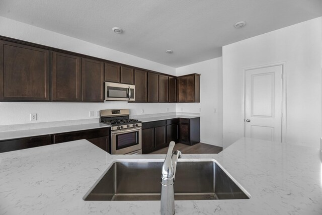 kitchen with dark brown cabinetry, light stone counters, stainless steel appliances, and a sink