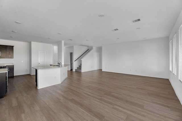 unfurnished living room featuring a sink, stairway, wood finished floors, and visible vents