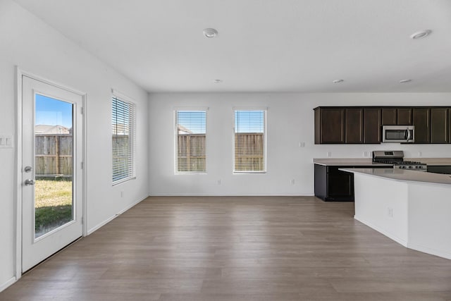 kitchen with dark brown cabinetry, appliances with stainless steel finishes, open floor plan, wood finished floors, and light countertops