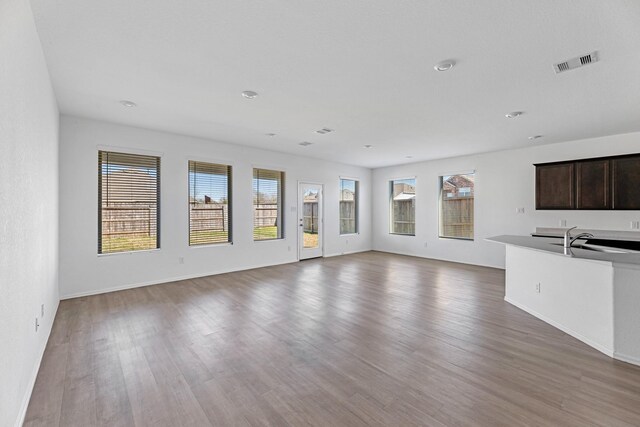 unfurnished living room with a sink, baseboards, visible vents, and wood finished floors