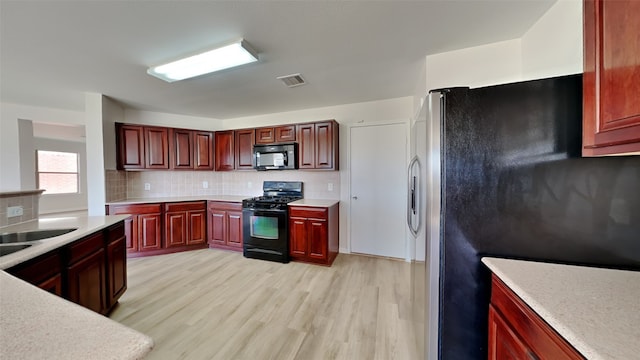 kitchen with reddish brown cabinets, black appliances, light countertops, and visible vents