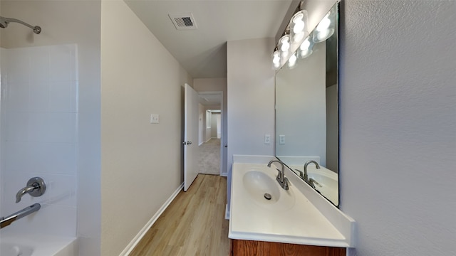 full bathroom with shower / bath combination, visible vents, vanity, wood finished floors, and baseboards