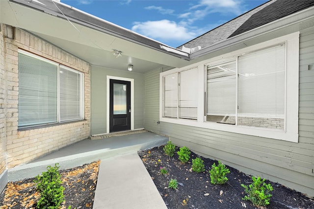 property entrance featuring brick siding and a shingled roof