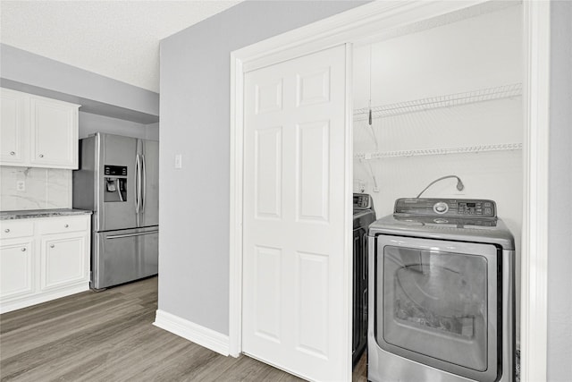 clothes washing area with baseboards, laundry area, light wood-style flooring, a textured ceiling, and independent washer and dryer