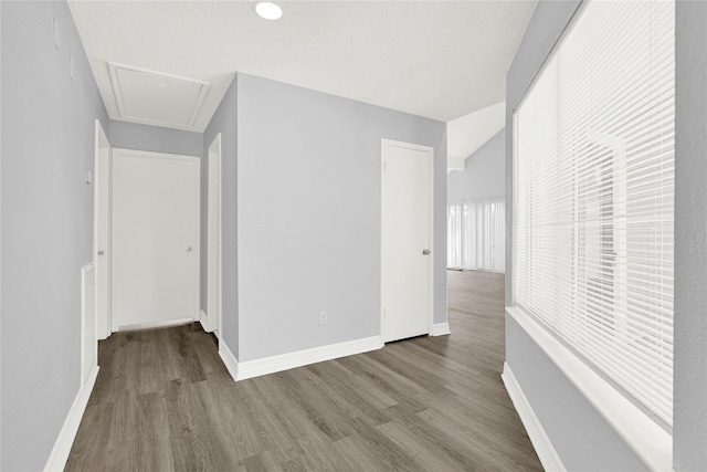 corridor with attic access, wood finished floors, baseboards, and a textured ceiling