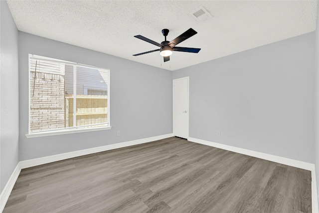 spare room featuring visible vents, a textured ceiling, baseboards, and wood finished floors