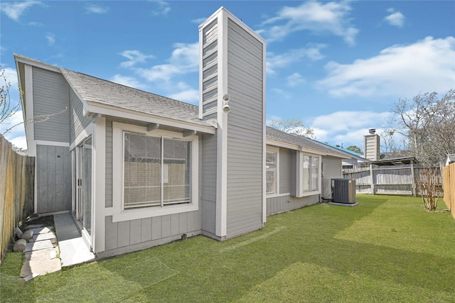 back of property featuring a fenced backyard, a yard, cooling unit, roof with shingles, and a chimney