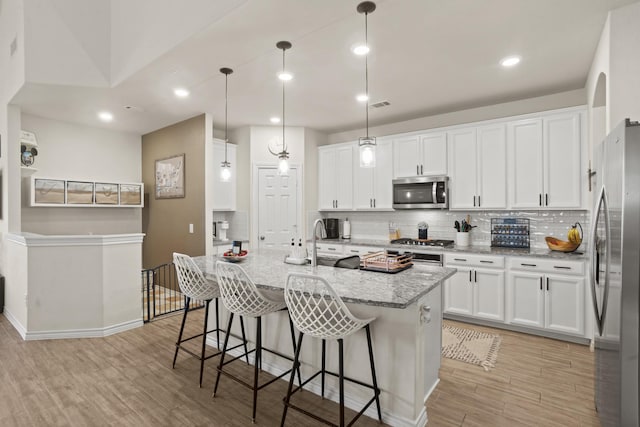 kitchen featuring stainless steel appliances, light wood-type flooring, white cabinets, and decorative backsplash