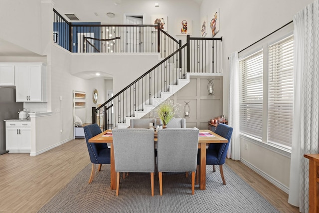 dining room with baseboards, a high ceiling, light wood finished floors, and stairs