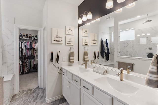 bathroom with double vanity, a marble finish shower, a walk in closet, and a sink