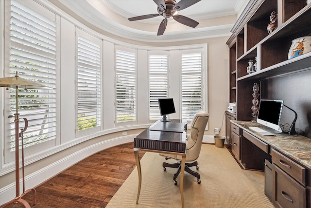 office space featuring ceiling fan, light wood-style flooring, baseboards, ornamental molding, and a tray ceiling