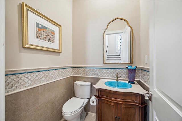 half bath with tile walls, a wainscoted wall, vanity, and toilet