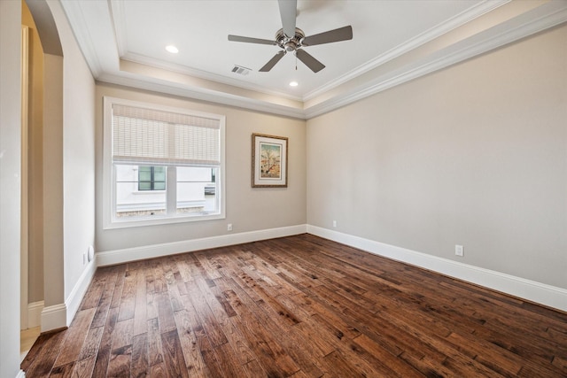 empty room featuring dark wood-type flooring, a tray ceiling, ornamental molding, and baseboards