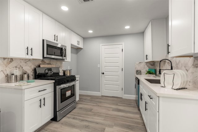 kitchen with stainless steel appliances, a sink, white cabinetry, light countertops, and light wood finished floors