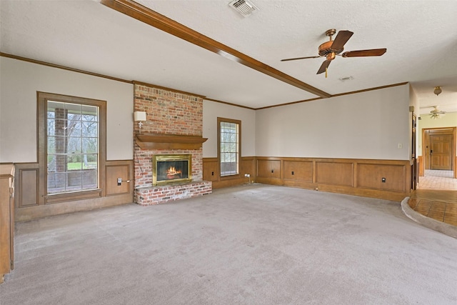 unfurnished living room with visible vents, a wainscoted wall, carpet flooring, a textured ceiling, and a fireplace