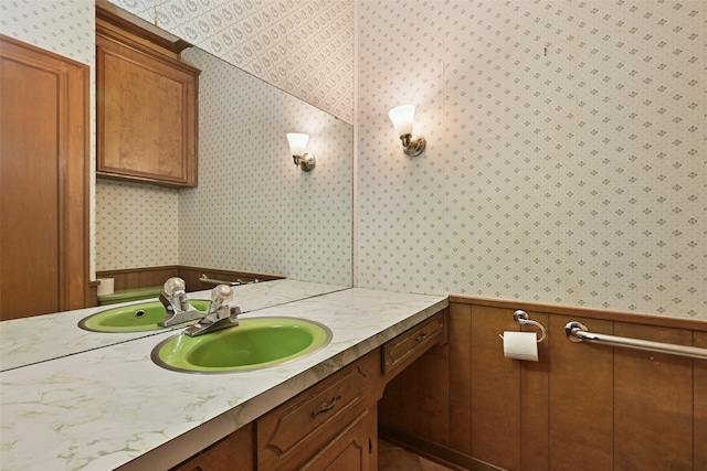 half bathroom with wainscoting, vanity, and wallpapered walls