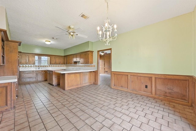 kitchen with light countertops, a wainscoted wall, visible vents, and ceiling fan with notable chandelier