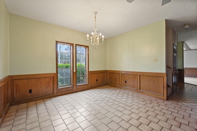 spare room with light tile patterned floors, a notable chandelier, a textured ceiling, and wainscoting