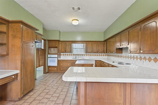 kitchen featuring open shelves, visible vents, a sink, oven, and a peninsula