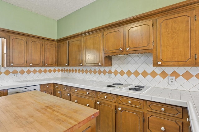 kitchen featuring brown cabinetry, white appliances, backsplash, and a textured ceiling