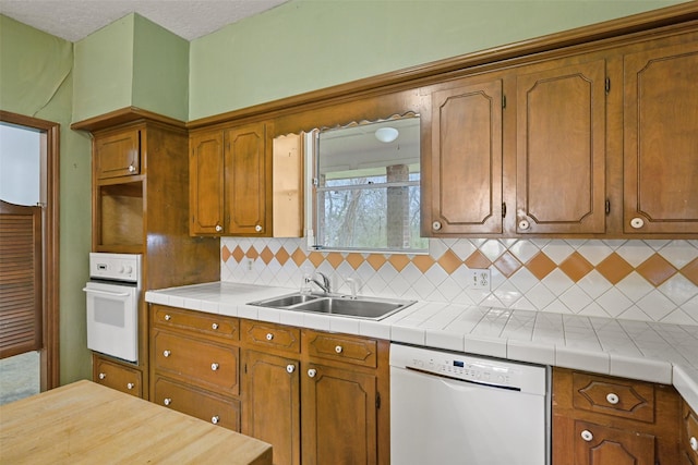 kitchen featuring white appliances, tasteful backsplash, brown cabinetry, and a sink