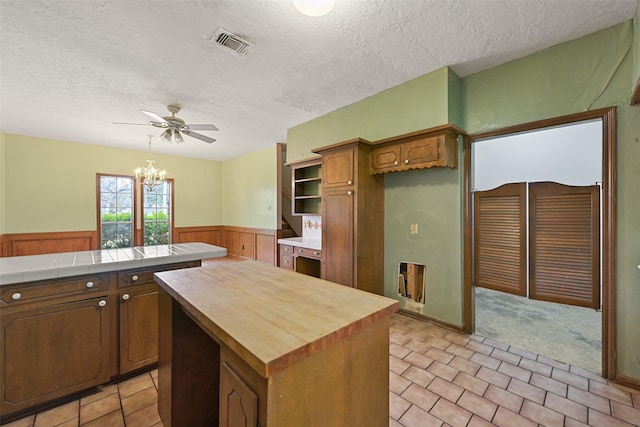 kitchen featuring a textured ceiling, a wainscoted wall, ceiling fan with notable chandelier, butcher block countertops, and visible vents