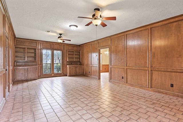 empty room with light tile patterned floors, wooden walls, built in features, a ceiling fan, and a textured ceiling