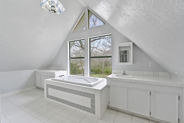 full bathroom featuring a textured ceiling, lofted ceiling, vanity, a bath, and tile patterned floors