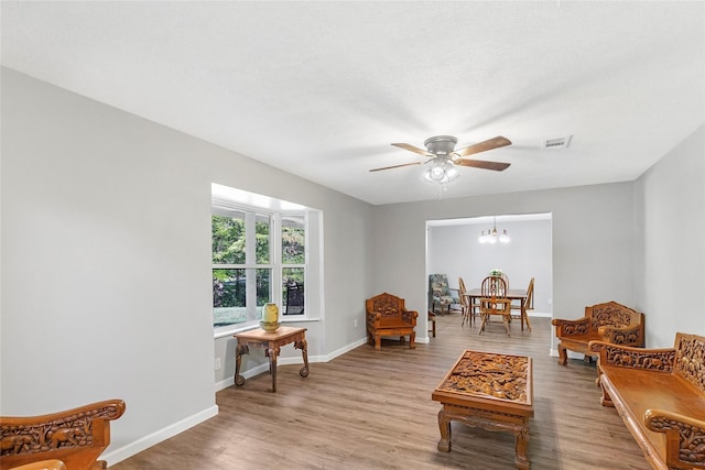 sitting room with ceiling fan with notable chandelier, light wood finished floors, visible vents, and baseboards