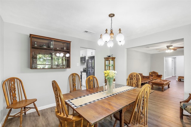 dining area featuring ceiling fan with notable chandelier, wood finished floors, visible vents, and baseboards