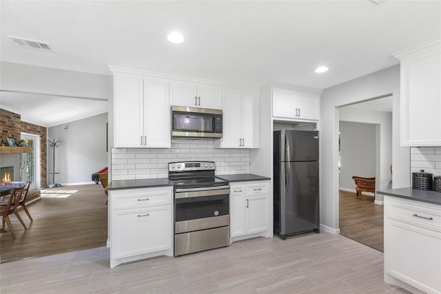 kitchen featuring stainless steel appliances, dark countertops, visible vents, and a brick fireplace