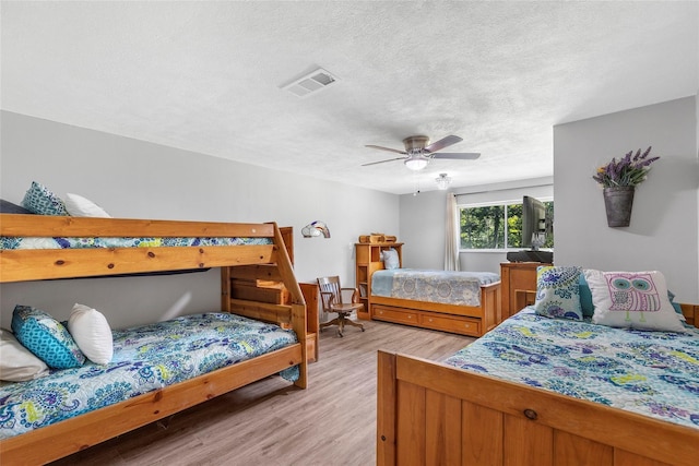 bedroom with light wood finished floors, a ceiling fan, visible vents, and a textured ceiling