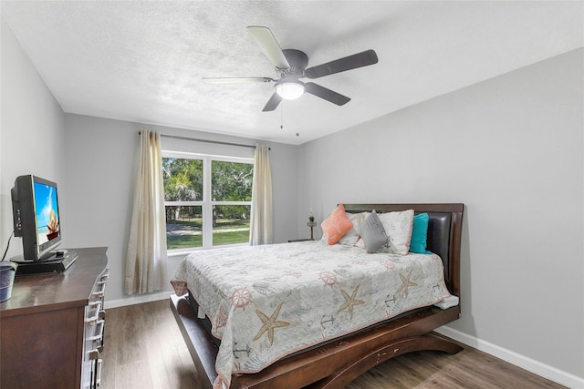 bedroom with ceiling fan, a textured ceiling, baseboards, and wood finished floors