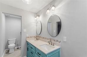 bathroom featuring baseboards, a sink, toilet, and double vanity