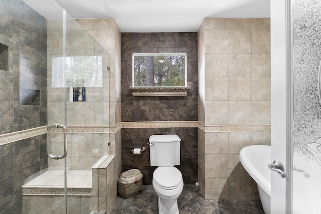 bathroom featuring toilet, tile patterned floors, a freestanding tub, a shower stall, and tile walls