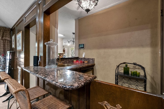 kitchen featuring a peninsula, dark brown cabinetry, dark stone counters, and a sink