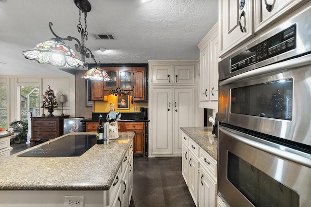 kitchen featuring a textured ceiling, stainless steel double oven, black electric cooktop, visible vents, and pendant lighting