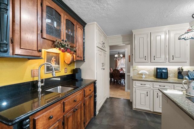 kitchen featuring tasteful backsplash, dark stone counters, glass insert cabinets, a sink, and a notable chandelier