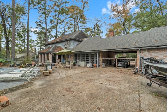 view of front of house featuring a patio area, a shingled roof, a chimney, and brick siding