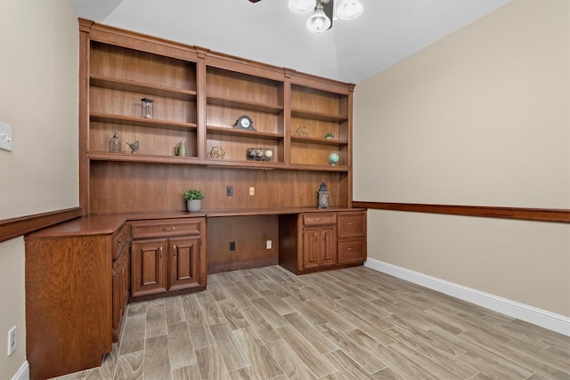 unfurnished office featuring built in desk, light wood-type flooring, a ceiling fan, and baseboards