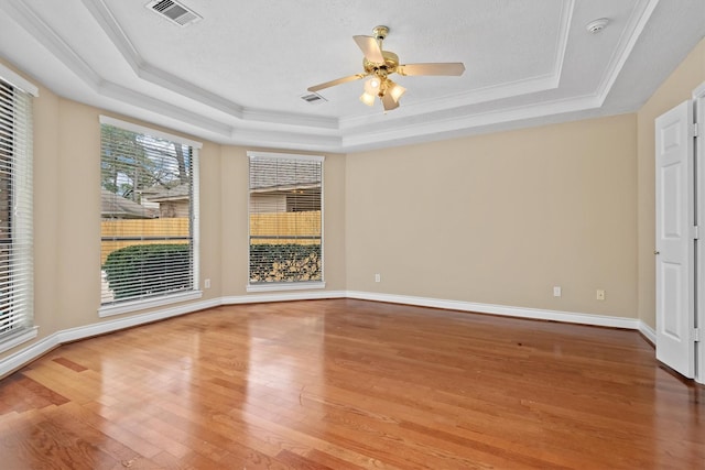 spare room with a tray ceiling, wood finished floors, visible vents, and baseboards