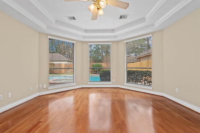 empty room with a raised ceiling, visible vents, and wood finished floors