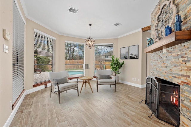 sitting room with light wood-style flooring, visible vents, crown molding, and a stone fireplace