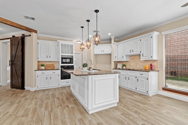 kitchen with white cabinets, a sink, black appliances, and a barn door