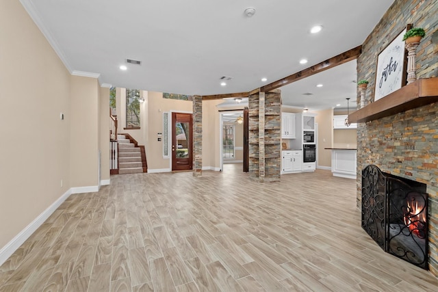 unfurnished living room featuring decorative columns, a fireplace, baseboards, and light wood-style flooring