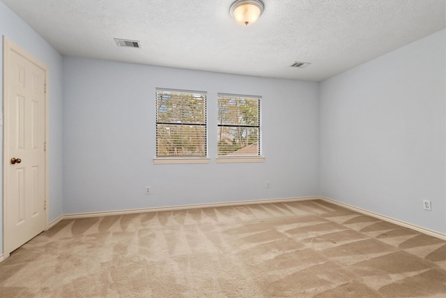 spare room with a textured ceiling, visible vents, and light colored carpet