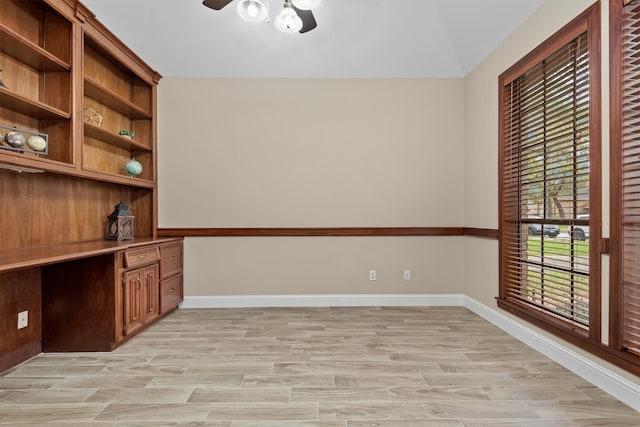 unfurnished office with light wood-style floors, built in desk, baseboards, and a ceiling fan