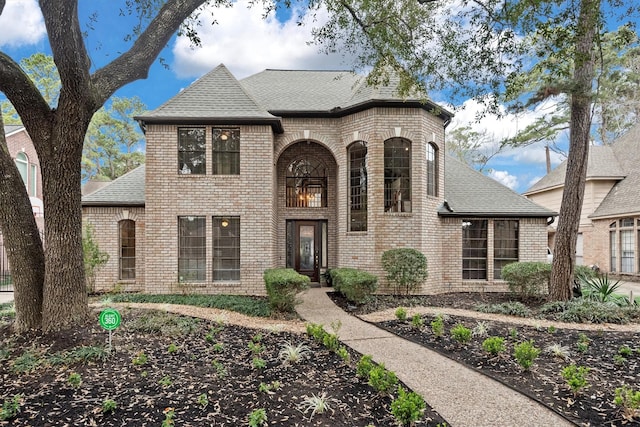 french provincial home with roof with shingles and brick siding