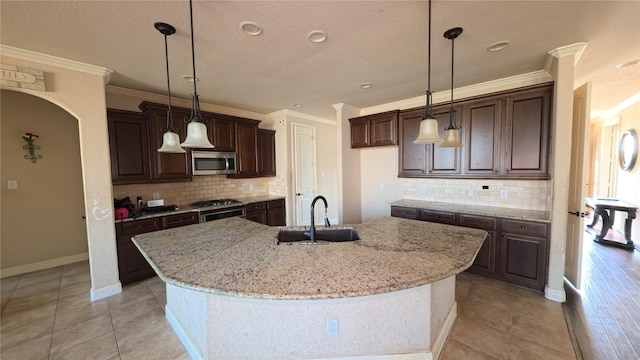 kitchen featuring light stone counters, crown molding, stainless steel microwave, a sink, and dark brown cabinetry